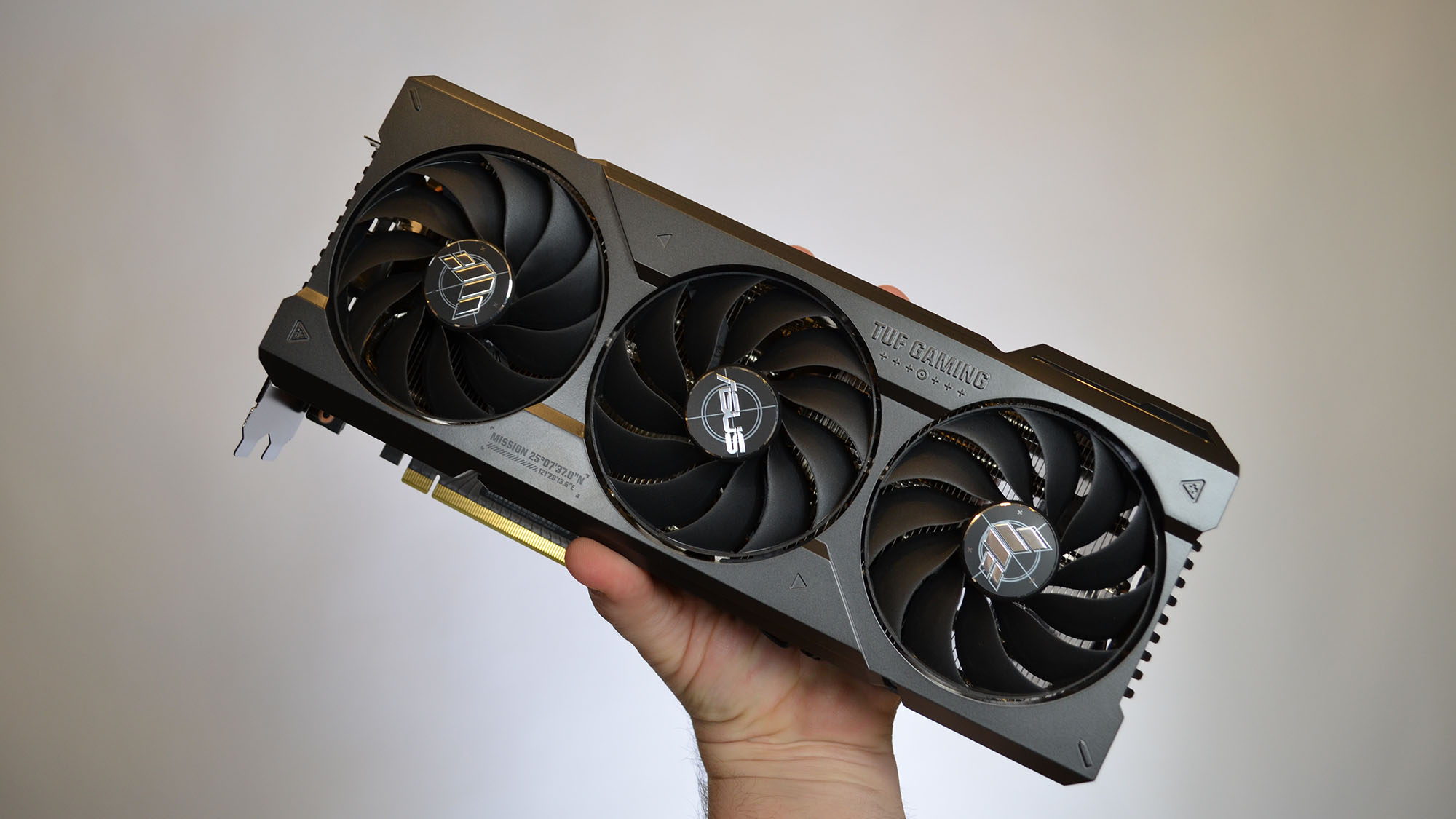 सफ़ेद स्पॉटलाइट पृष्ठभूमि में आसुस टग गेमिंग GeForce RTX 4070 Ti पकड़े हुए एक आदमी का हाथ